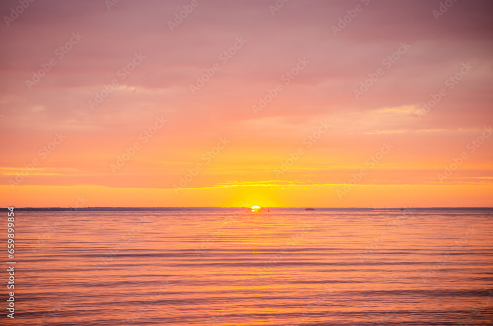 Beautiful bright picturesque dawn, sunrise on a river or sea in summer, through of clouds in the sky rays of red and orange color