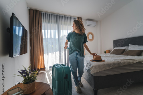 A young woman in a hat with a suitcase check in a hotel room. Booking and Accommodation travel concept
