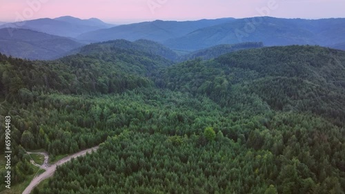 the camera flies over the forest in the mountains opens a view of the road that leads to the church on the top of the mountain. Ukrainian Carpathians, evening, summer, 4K