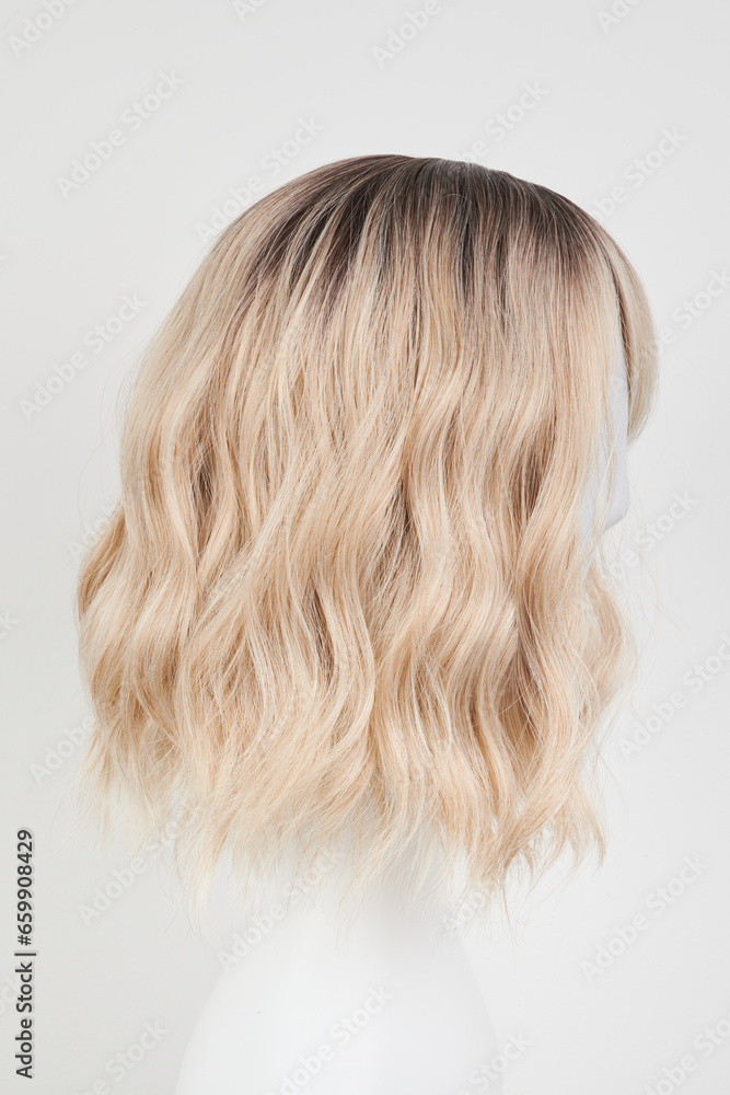 Naklejka premium Natural looking blonde fair wig on white mannequin head. Middle length hair cut on the plastic wig holder isolated on white background, side view.