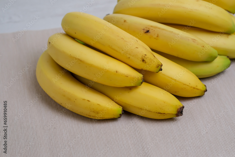 Bunch of organic banana fruits isolated on natural background. Barely ripe yellow bananas on beige linen fabric on the table in the kitchen. Bunch of organic banana fruits isolated on natural background. Barely ripe yellow bananas on beige linen fabric on the table in the kitchen.