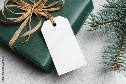 Blank gift tag card mockup with christmas gift box on grey background, white label with copy space for design presentation