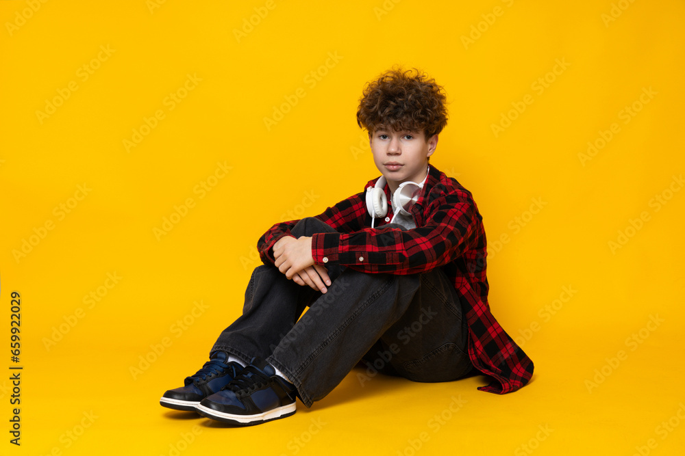 Curly boy teenager sitting on the floor, on a yellow background. Curly boy teenager sitting on the floor, on a yellow background.