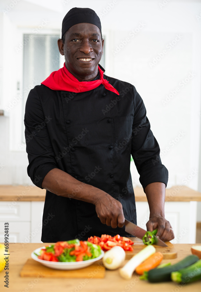 Cheerful chef in black uniform cutting vegetables for salad in home kitchen Cheerful chef in black uniform cutting vegetables for salad in home kitchen