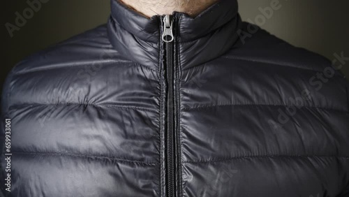 A male hand zips up a black down filled jacket