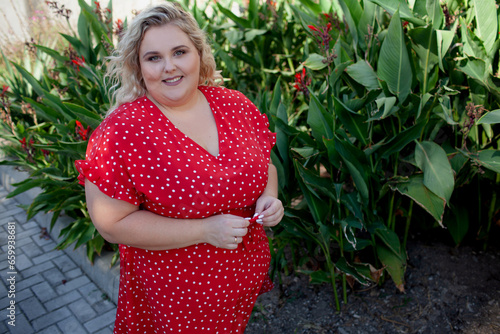 Portrait of a beautiful woman holds phone in hand, walks in the street of the city. Plus size woman dressed fashion outfit,  red dress, posing outdoor