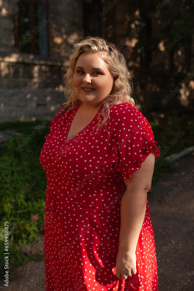 Portrait of a beautiful woman holds phone in hand, walks in the street of the city. Plus size woman dressed fashion outfit, red dress, posing outdoor Portrait of a beautiful woman holds phone in hand, walks in the street of the city. Plus size woman dressed fashion outfit, red dress, posing outdoor