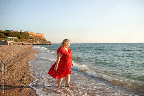 Plus size woman walking in the beach. The overweight woman dressed red dress. Happy moment