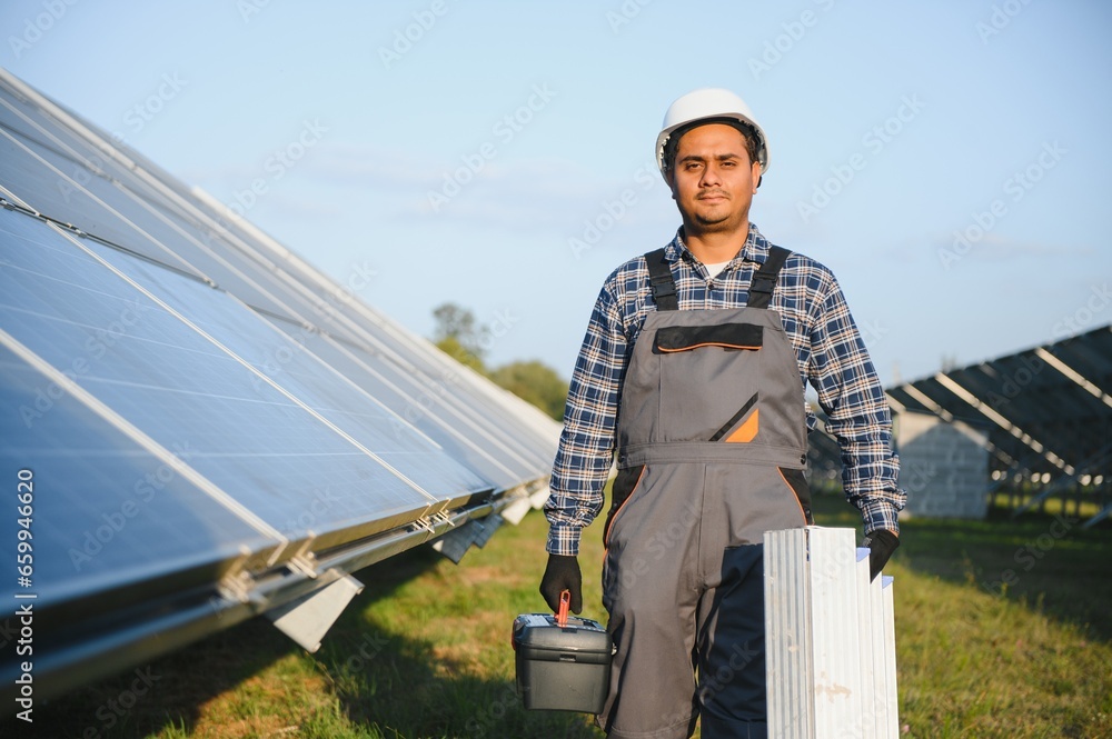 Indian man in uniform on solar farm. Competent energy engineer controlling work of photovoltaic cells