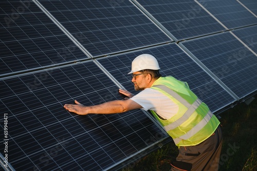 Side view of male worker installing solar modules and support structures of photovoltaic solar array.