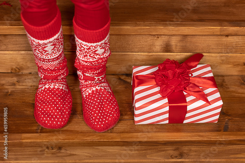 Foot in Christmas red socks next to a Christmas gift on a wooden background