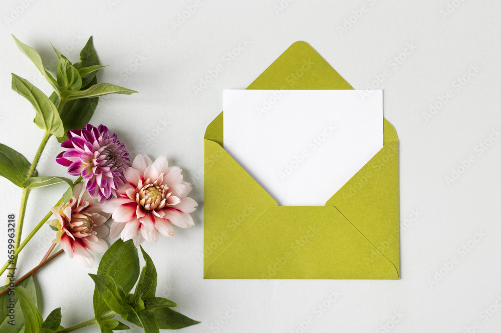 Green envelope with clean white sheet of paper for your text and autumn flowers dahlias on gray background. Invitation to the holidays. Flat lay. Green envelope with clean white sheet of paper for your text and autumn flowers dahlias on gray background. Invitation to the holidays. Flat lay.