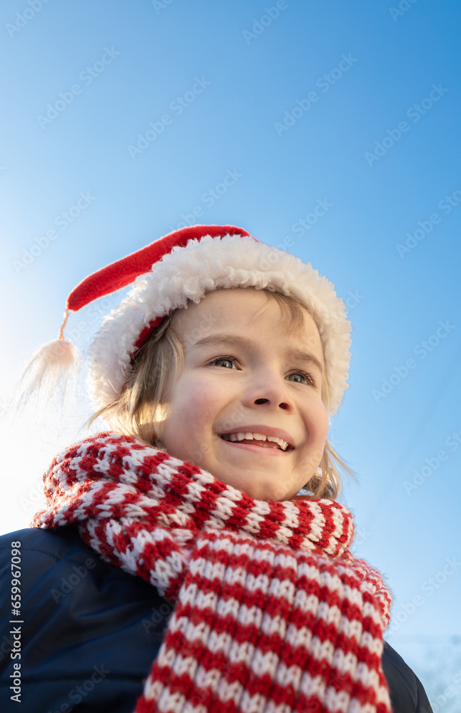 face of a child 6 - 7 years old, in a striped red scarf and Santa's hat against the blue sky on a sunny cold day. Winter walks and entertainment. happy childhood, winter holidays face of a child 6 - 7 years old, in a striped red scarf and Santa's hat against the blue sky on a sunny cold day. Winter walks and entertainment. happy childhood, winter holidays