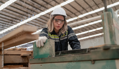 Confident female worker standing in lumber warehouse of hardwood furniture factory inspecting production machine. Serious female technician, engineer busy working with tool in woodwork manufacturing.