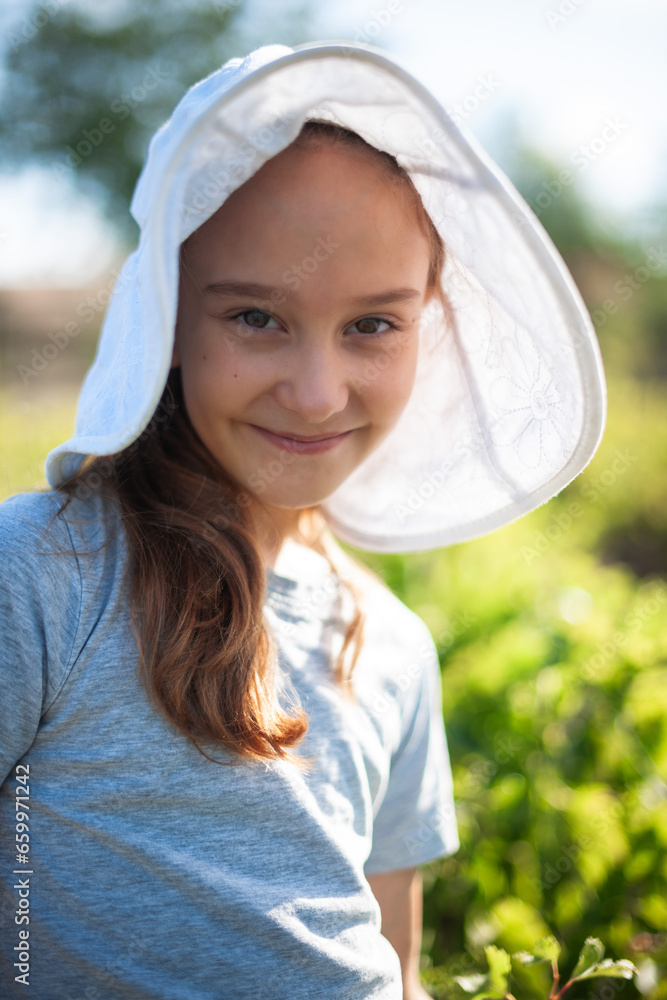 portrait of a smilling girl in the summer garden. The girl is wearing a large white hat. Duvochka smiles and looks at the camera portrait of a smilling girl in the summer garden. The girl is wearing a large white hat. Duvochka smiles and looks at the camera