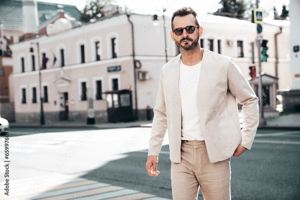 Portrait of handsome confident stylish hipster lambersexual model. Sexy modern man dressed in elegant suit. Fashion male posing in the street background in Europe city at sunset. In sunglasses Portrait of handsome confident stylish hipster lambersexual model. Sexy modern man dressed in elegant suit. Fashion male posing in the street background in Europe city at sunset. In sunglasses