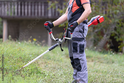 Man mowing the grass at his garden by using string trimmer with protective equipment.