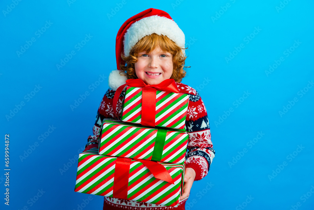 Photo of good mood cute little boy dressed ugly pullover x-mas hat getting presents isolated blue color background Photo of good mood cute little boy dressed ugly pullover x-mas hat getting presents isolated blue color background