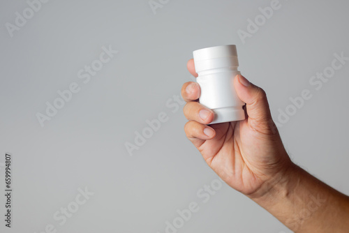 The man's hand held a medicine bottle containing antibiotics against a white background.