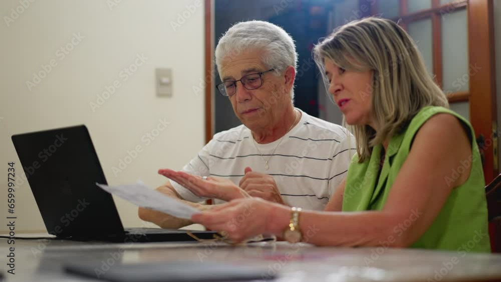Mature Couple Discussing Finances, Paying Debt Online at Kitchen Table Mature Couple Discussing Finances, Paying Debt Online at Kitchen Table