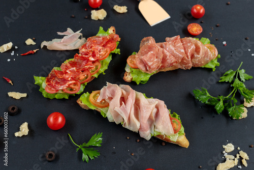 Bruschetta with salami, chorizo and prosciutto on a black background with ingredients for cooking. photo