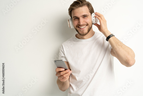 Caucasian young student man freelancer listening to the music in headphones, choosing sound track, song, playlist, podcast on phone isolated in white background.
