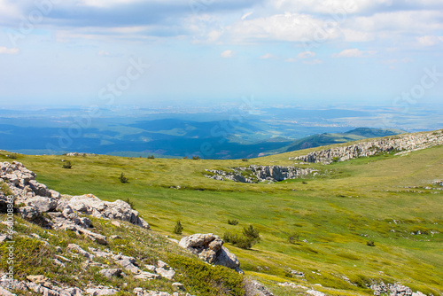 plateau in the mountains of Crimea covered with grass with stones in the foreground, distant hills, sky and clouds in the background