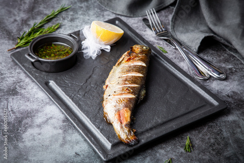 River trout baked in josper with sauce and lemon on a dark background