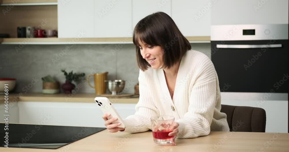 A Caucasian woman is engrossed in texting on her phone while casually sipping juice from a glass. Her relaxed multitasking reflects her ability to stay connected while enjoying a refreshing drink. A Caucasian woman is engrossed in texting on her phone while casually sipping juice from a glass. Her relaxed multitasking reflects her ability to stay connected while enjoying a refreshing drink.