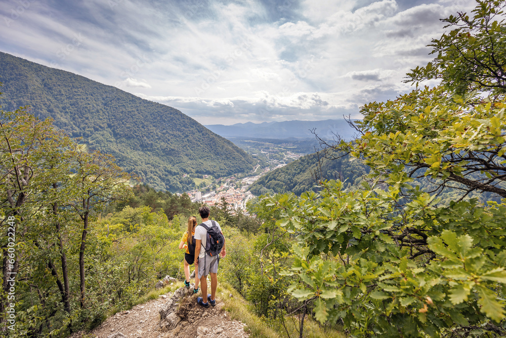 Young, embraced couple enjoying the fantastic mountain and valley panorama, taking a break on a viewpoint after a hike on a sunny summer day