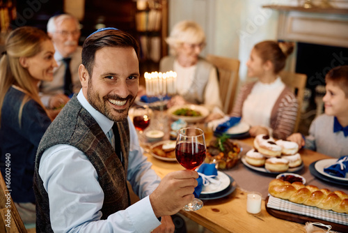 Happy Jewish man toasting during family meal on Hanukkah at looking at camera.
