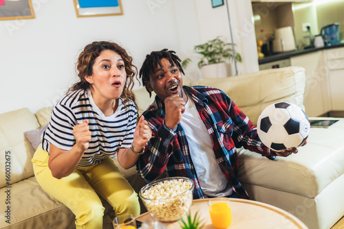 African American husband and latina wife watching a football game on television from the comfort of their home.