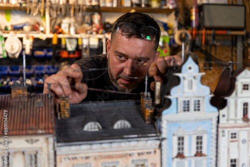 Model maker man working at scale model of miniature building in his workshop full of tools