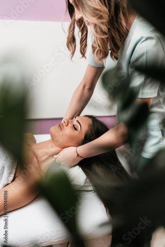 Beautiful young adult brunette receiving professional relaxation massage treatment at beauty spa salon.