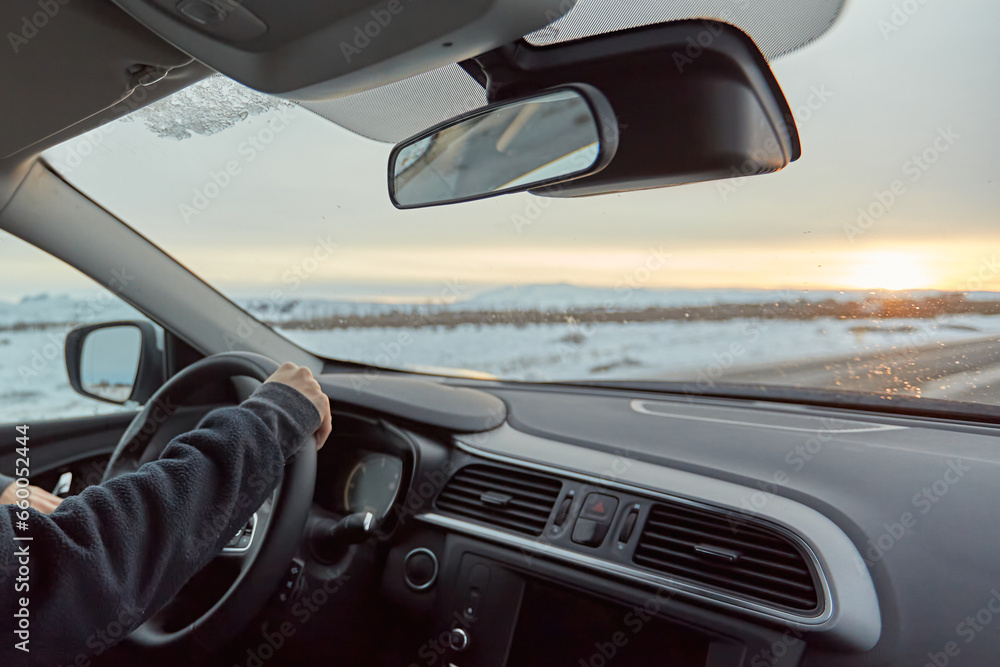 Man driving a car along a snowy ocean shore, highlighting the vehicle's modern design and the vast, serene seascape