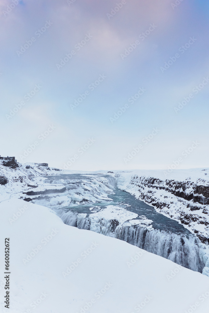 Stunning snow-covered waterfall in Iceland, captured with grandeur, sunlight adding a soft glow to the serene beauty