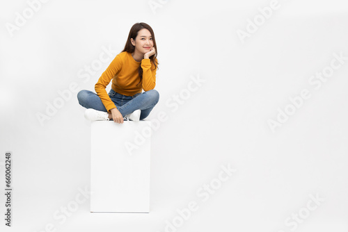 Smiling young Asian woman sitting on white box isolated on white background