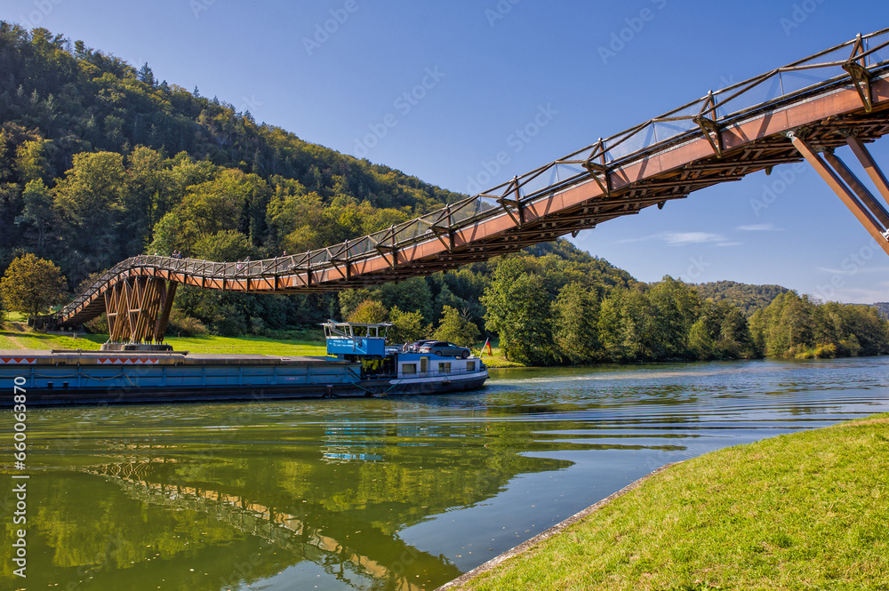 a barge is passing under the second longest wooden bridge in europe called tatzlwurm on the main-danube canal in sunny weather and beautiful reflections in the water