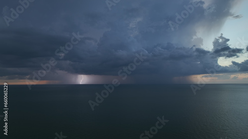 Dark ominous thunderstorm clouds forming on overcast sky during heavy rainfall season over ocean surface at sunset