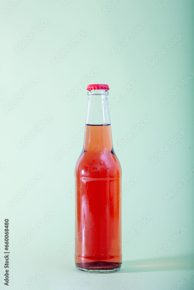 A red liquid-filled bottle against a light, dry green backdrop. A red liquid-filled bottle against a light, dry green backdrop.