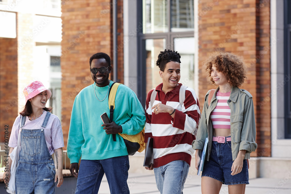Fototapeta premium Multiethnic group of young students walking in row together outdoors on college campus and smiling happily