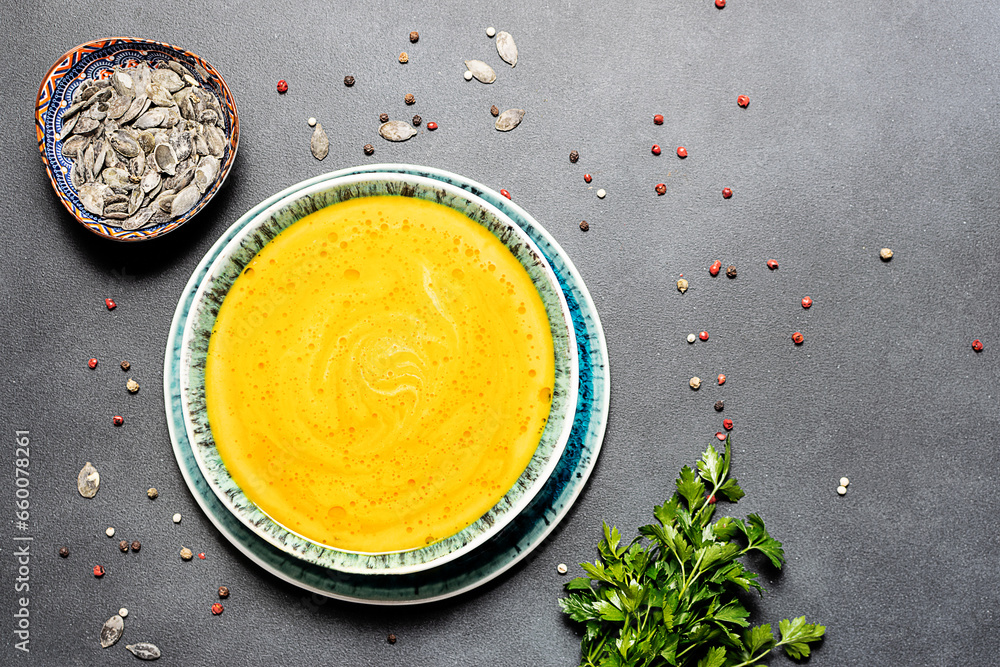Aromatic hot pumpkin soup with spices, seeds and parsley on black stone table top view. Healthy tasty food concept. Aromatic hot pumpkin soup with spices, seeds and parsley on black stone table top view. Healthy tasty food concept.