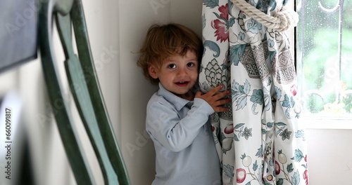 Cute toddler boy hiding behind curtain photo