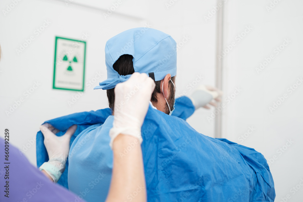 Doctor being helped to put on the sterile gown to perform the surgery. Concept: surgical, operation, sterility Doctor being helped to put on the sterile gown to perform the surgery. Concept: surgical, operation, sterility