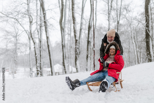 Senior couple having fun during cold winter day, sledding down the hill. Winter vacation in the mountains. Wintry landscape.