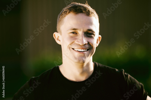 Close up portrait of smiling European man 26 years old outdoors in summer with blurred background.
