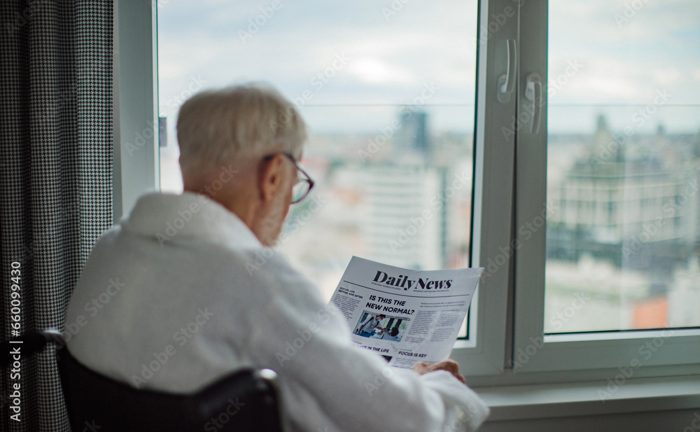 Elderly man in a wheelchair reading the newspaper in his robe in the morning. Concept of loneliness and dependence of retired people. Elderly man in a wheelchair reading the newspaper in his robe in the morning. Concept of loneliness and dependence of retired people.