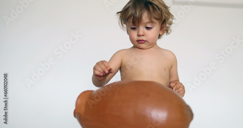 Toddler boy saving money inserting coins inside piggy bank