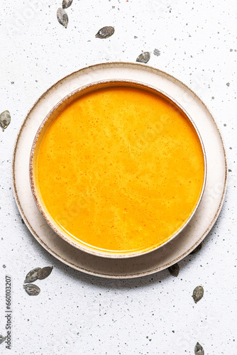Autumn hot pumpkin soup with cream, parsley and pumpkin seads on white marble table top view. Vertical image.
