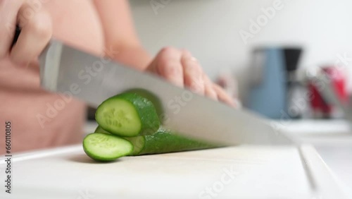 Woman's hands using a kitchen knife cut fresh cucumber on cutting board photo